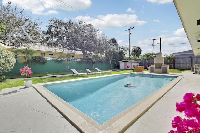 view of swimming pool featuring an outbuilding, a fenced backyard, a patio, and an outdoor fireplace