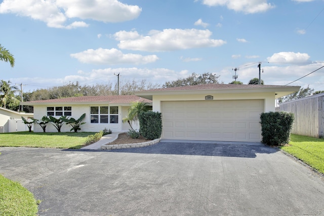 ranch-style home with a garage, fence, driveway, stucco siding, and a front lawn