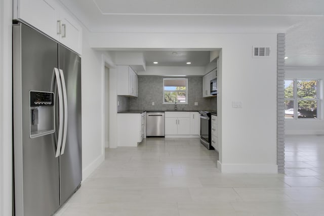 kitchen with visible vents, white cabinets, dark countertops, stainless steel appliances, and a sink