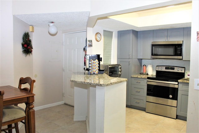 kitchen with backsplash, stainless steel appliances, light stone counters, a textured ceiling, and light tile patterned flooring