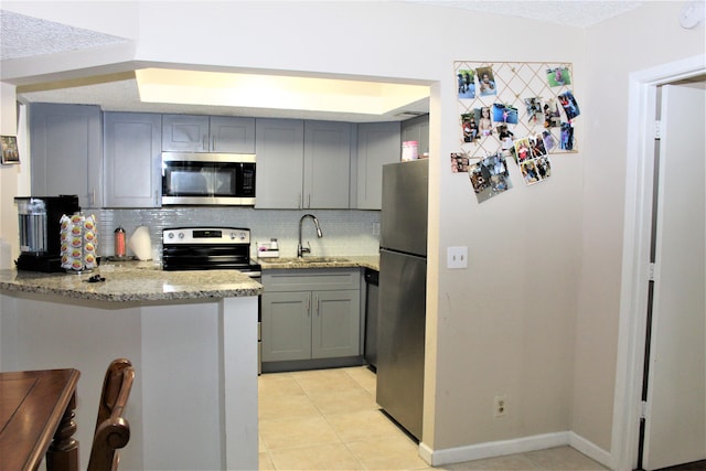 kitchen featuring stainless steel appliances, light stone countertops, sink, and backsplash