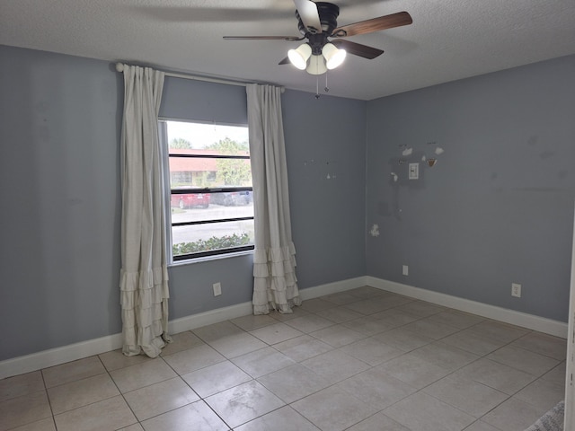 empty room with a ceiling fan, light tile patterned floors, baseboards, and a textured ceiling