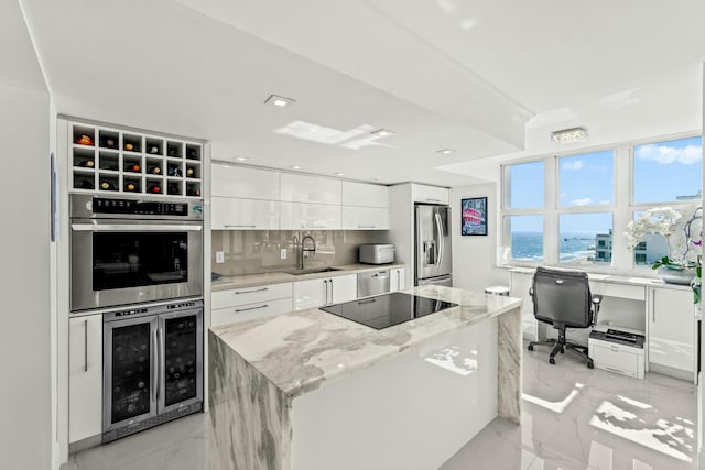 kitchen with white cabinets, wine cooler, appliances with stainless steel finishes, a center island, and a sink