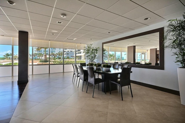 dining room featuring light tile patterned floors, a drop ceiling, and baseboards