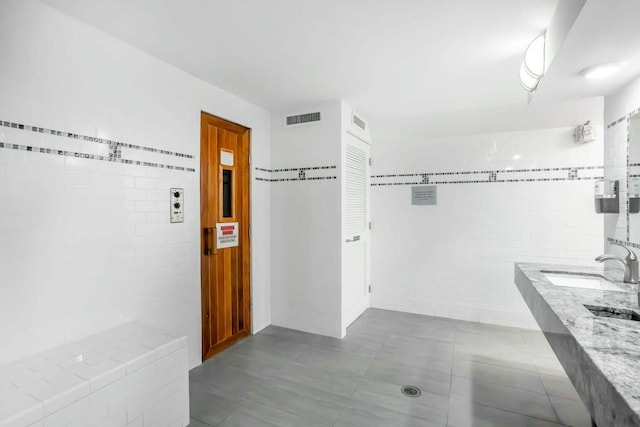 bathroom with visible vents, a sink, and tile walls