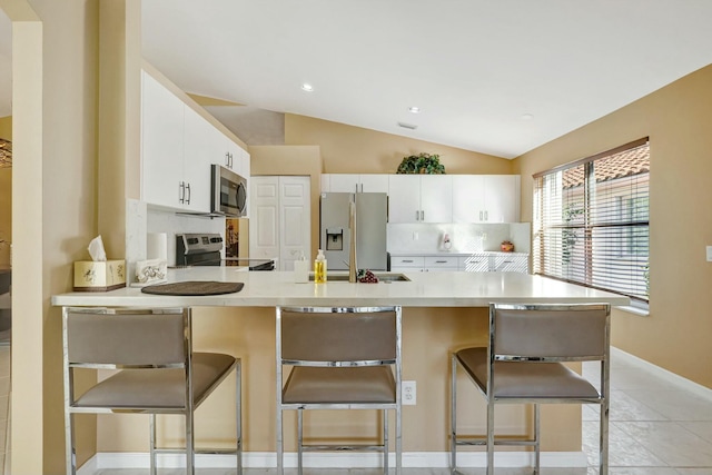 kitchen featuring white cabinetry, kitchen peninsula, stainless steel appliances, vaulted ceiling, and a breakfast bar area