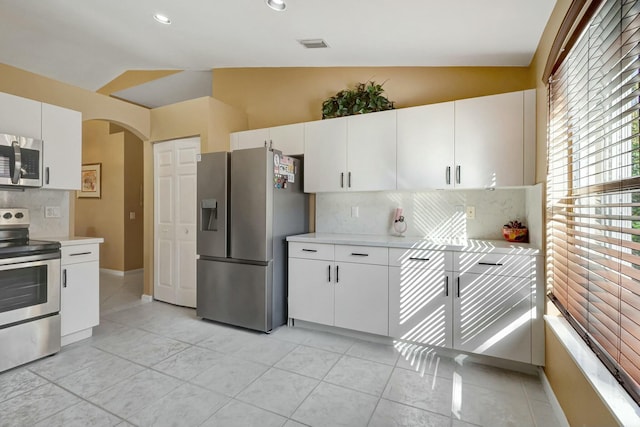 kitchen with decorative backsplash, appliances with stainless steel finishes, white cabinets, and lofted ceiling