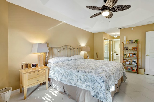 tiled bedroom with a tray ceiling, ceiling fan, and connected bathroom