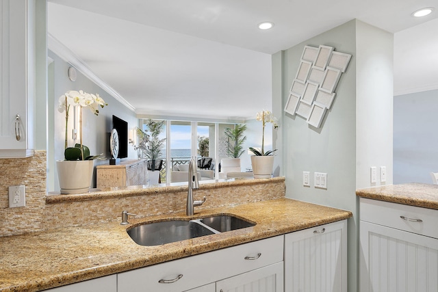 kitchen featuring light stone counters, a sink, white cabinetry, ornamental molding, and backsplash