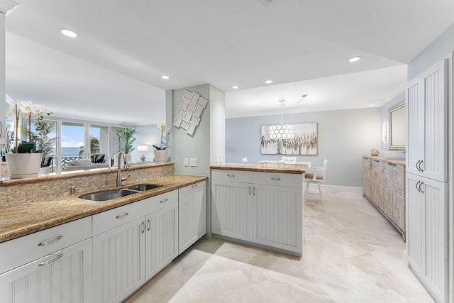 kitchen with light stone counters, recessed lighting, a sink, and a peninsula