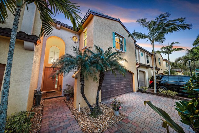 mediterranean / spanish home featuring a garage, a tiled roof, decorative driveway, and stucco siding