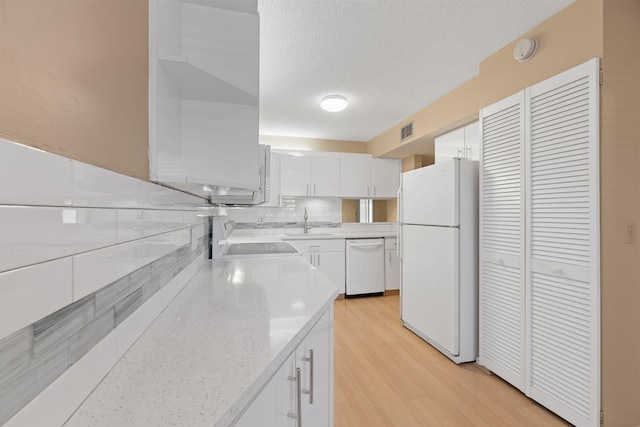 kitchen with white appliances, visible vents, a sink, white cabinetry, and backsplash