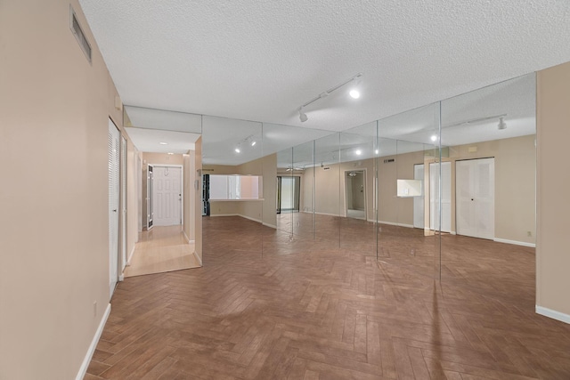 spare room featuring a textured ceiling, rail lighting, visible vents, and baseboards