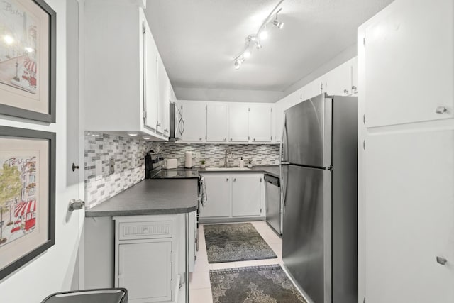 kitchen with light tile patterned floors, white cabinets, appliances with stainless steel finishes, decorative backsplash, and dark countertops