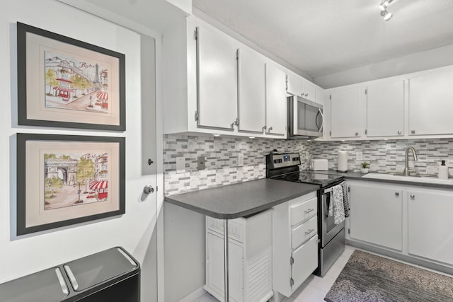 kitchen with stainless steel appliances, a sink, white cabinets, backsplash, and dark countertops