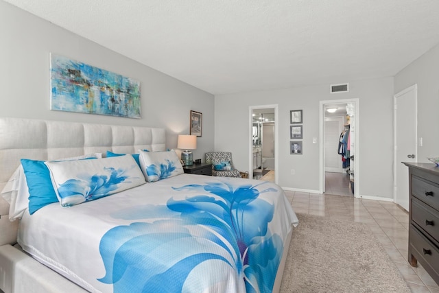 bedroom featuring light tile patterned floors, visible vents, baseboards, a spacious closet, and ensuite bath