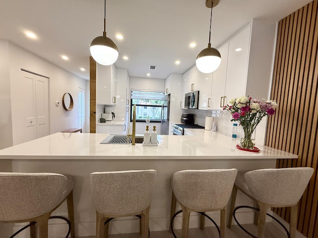 kitchen featuring white cabinetry, stainless steel appliances, kitchen peninsula, hanging light fixtures, and tasteful backsplash