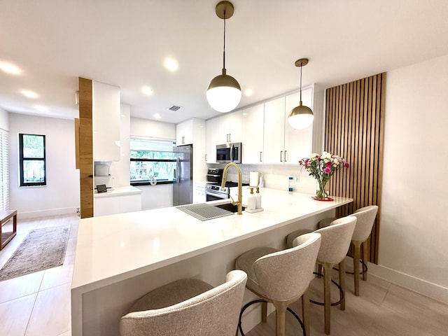 kitchen featuring kitchen peninsula, stainless steel appliances, a healthy amount of sunlight, white cabinets, and pendant lighting