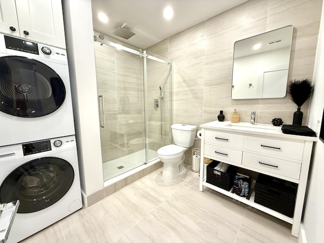 bathroom with tile walls, vanity, stacked washer / drying machine, and walk in shower