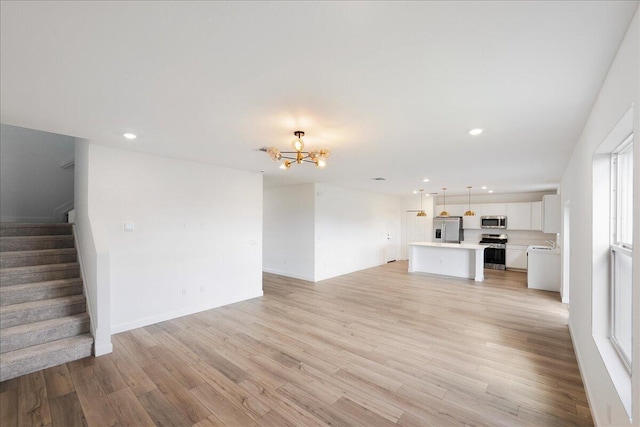 unfurnished living room featuring a notable chandelier, recessed lighting, stairway, a sink, and light wood-type flooring