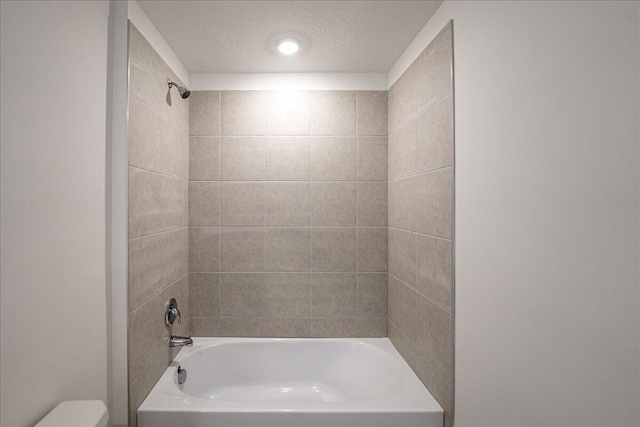 bathroom with a textured ceiling, toilet, and shower / bathtub combination