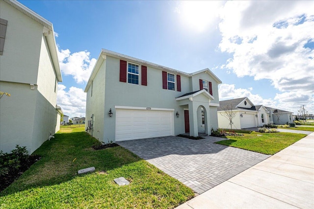 traditional-style home featuring decorative driveway, an attached garage, a front lawn, and stucco siding