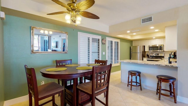 tiled dining space with a tray ceiling and ceiling fan