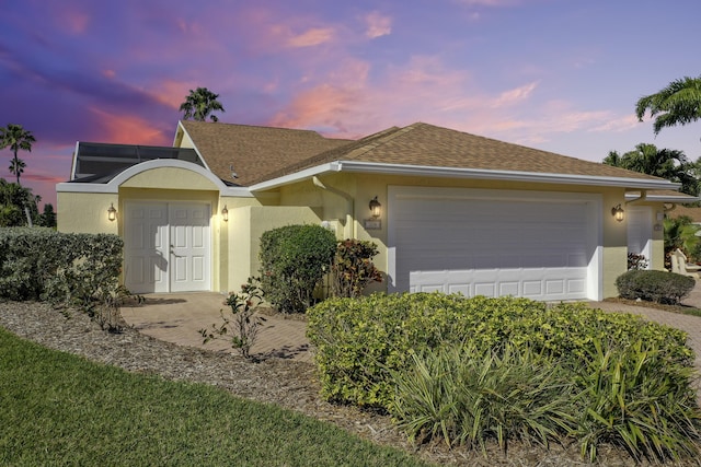 ranch-style home featuring an attached garage, a shingled roof, and stucco siding