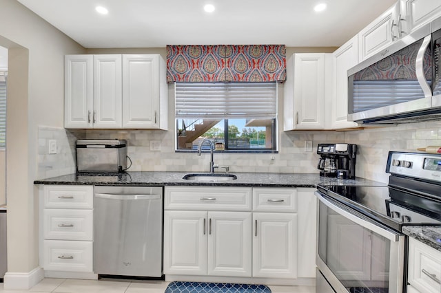 kitchen featuring stainless steel appliances, white cabinets, backsplash, sink, and dark stone countertops