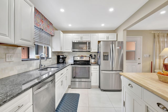 kitchen featuring stainless steel appliances, white cabinets, light tile patterned floors, sink, and dark stone countertops