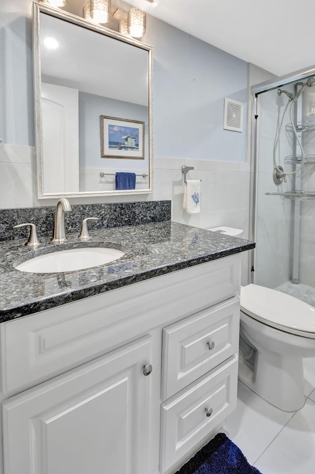 bathroom with tile walls, toilet, vanity, and a shower with shower door