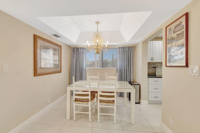 dining area with light tile patterned flooring, an inviting chandelier, and a tray ceiling