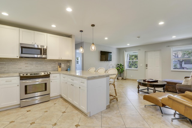 kitchen with appliances with stainless steel finishes, white cabinetry, pendant lighting, and kitchen peninsula