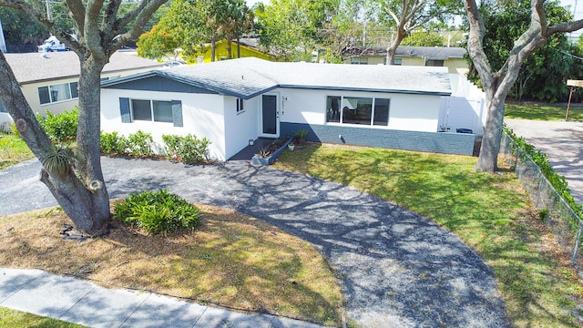 ranch-style home with a front yard, fence, driveway, and stucco siding