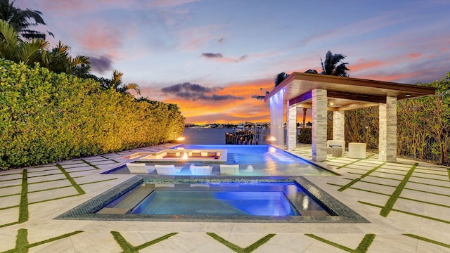 pool at dusk featuring an outdoor pool, an in ground hot tub, and a patio area