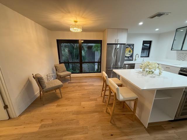 kitchen with a center island, white cabinetry, decorative light fixtures, light hardwood / wood-style floors, and stainless steel refrigerator