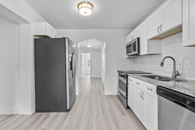 kitchen featuring appliances with stainless steel finishes, sink, light wood-type flooring, white cabinets, and light stone countertops