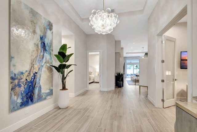 interior space with wood finish floors, an inviting chandelier, a raised ceiling, and baseboards