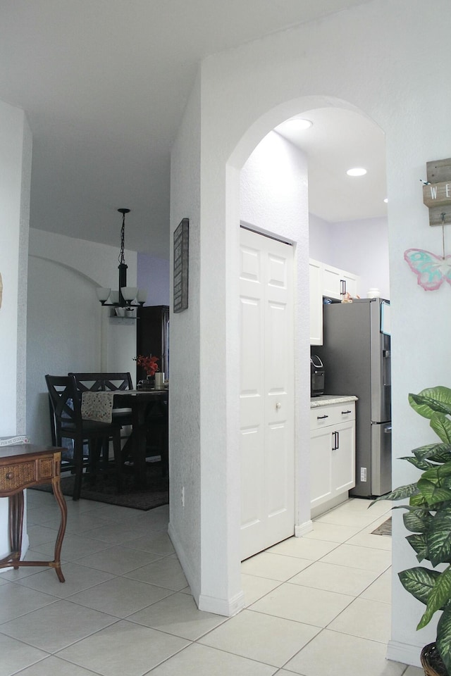 hall featuring light tile patterned flooring, arched walkways, and a notable chandelier