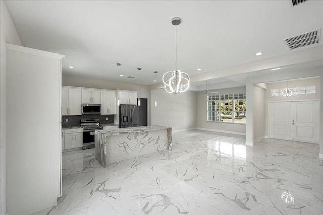 kitchen featuring appliances with stainless steel finishes, white cabinetry, hanging light fixtures, light stone countertops, and decorative backsplash