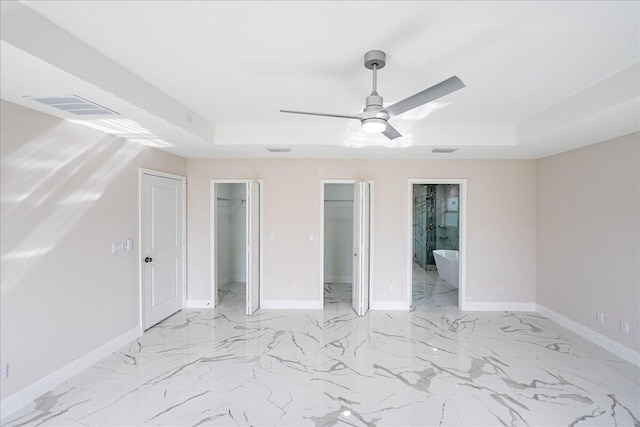 unfurnished bedroom featuring connected bathroom, ceiling fan, a tray ceiling, and a spacious closet