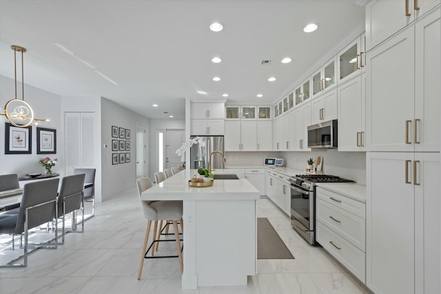 kitchen with a center island with sink, white cabinets, appliances with stainless steel finishes, light countertops, and pendant lighting