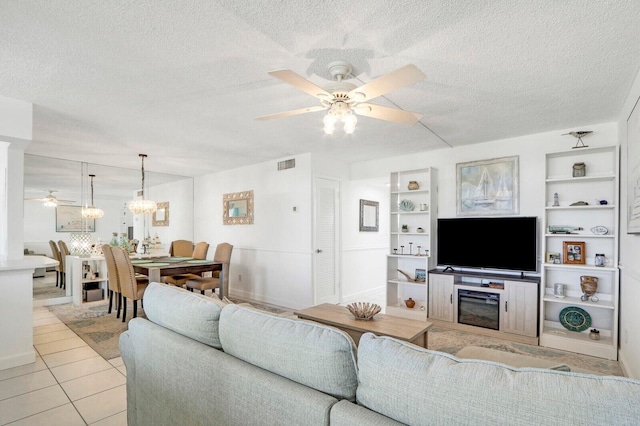 living area featuring built in shelves, ceiling fan with notable chandelier, a textured ceiling, and light tile patterned floors