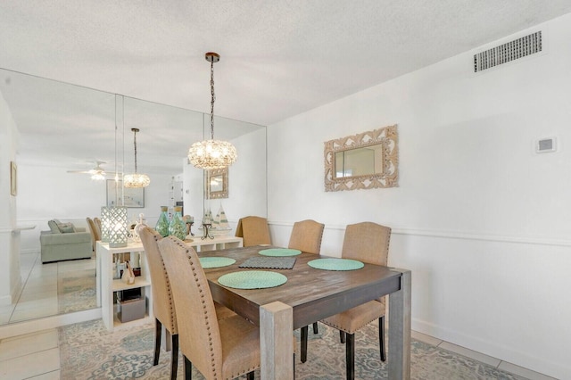 dining area with light tile patterned floors, a textured ceiling, ceiling fan with notable chandelier, and visible vents