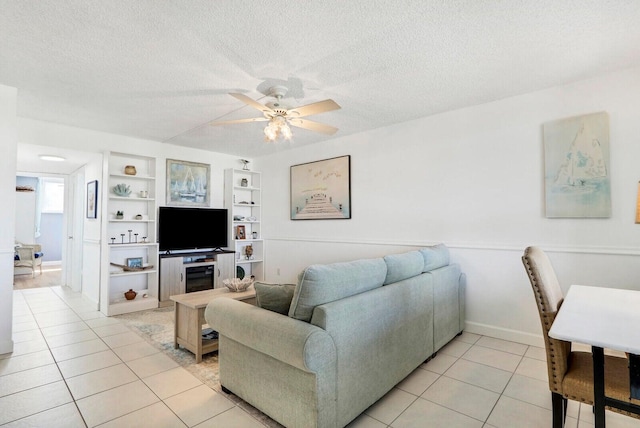 living room with a ceiling fan, built in features, a textured ceiling, and light tile patterned flooring