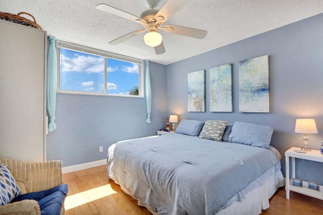 bedroom featuring ceiling fan, a textured ceiling, baseboards, and wood finished floors