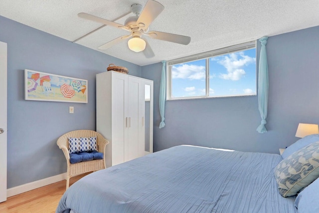 bedroom featuring ceiling fan, a textured ceiling, baseboards, and wood finished floors