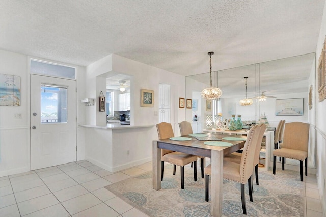 dining room featuring ceiling fan with notable chandelier, light tile patterned floors, a textured ceiling, and baseboards