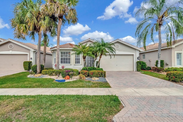 view of front of home featuring decorative driveway, stucco siding, a garage, a tiled roof, and a front lawn