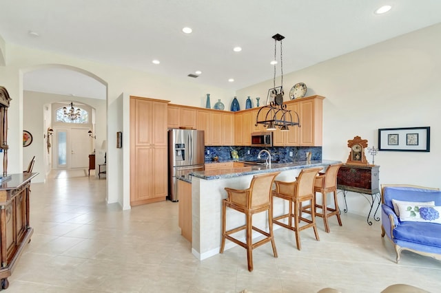 kitchen featuring arched walkways, an inviting chandelier, appliances with stainless steel finishes, dark stone counters, and a peninsula